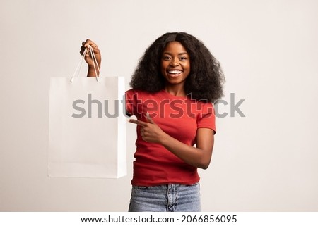 Portrait Of Happy Black Woman Pointing At Blank Shopping Bag With Copy Space For Your Design And Smiling At Camera, Beautiful African American Female Showing Free Place For Advertisement Or Branding