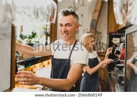 Confident smiling middle-aged small business owners barista bartenders waiters in blue aprons brewing coffee working preparing drinks orders for customers at the bar counter in restaurant cafe. Royalty-Free Stock Photo #2066868149