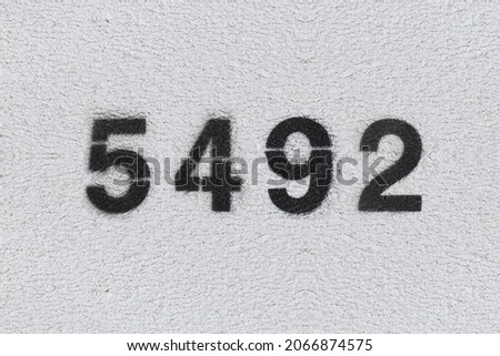 Black Number 5492 on the white wall. Spray paint. Number five thousand four hundred ninety two.