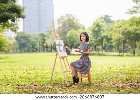 Asian kid painting on the canvas in the park. Happy child girl drawing a picture outdoors