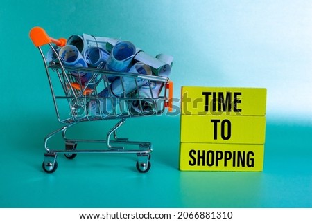 'Time to shopping' concept, Shopping trolley with dollar and euro banknotes, wooden blocks with 'time to shopping' written on it.