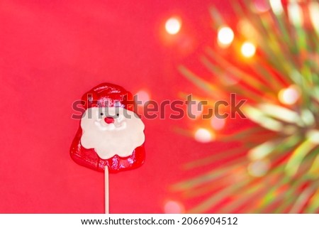 Christmas candy cane on a red background in the form of Santa Claus, Santa Claus with a blurred Christmas tree branch with a bokeh. Christmas New Year card, banner. Flat lay, copyspace