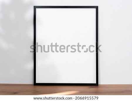 mockup black frame with light and shadow tree on wood table. empty white frame.