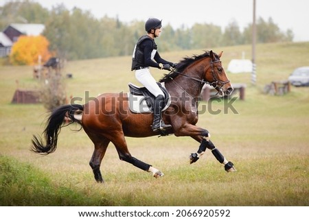 portrait of rider man and black stallion horse galloping during eventing cross country competition in autumn Royalty-Free Stock Photo #2066920592