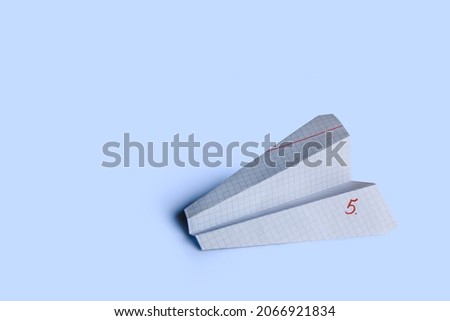 The paper airplane is made of a squared notebook sheet. Traditional origami from paper. Children's creativity. Horizontal photo with a field for text.