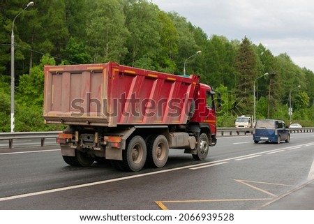 A truck on the road. Construction equipment is driving on the highway. A car with a body to carry loose material. A red truck.