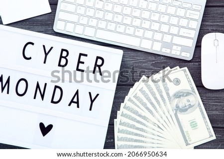 Lightbox with inscription Cyber Monday, dollar banknotes and keyboard on black wooden background