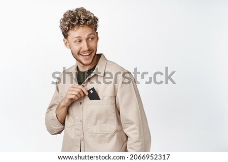 Happy blond guy put credit card in his pocket, smiling and looking behind at empty space, promo text, concept of shopping and money Royalty-Free Stock Photo #2066952317