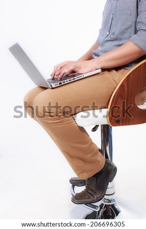  Young man sitting on a high chair and working on a laptop isolated on white background