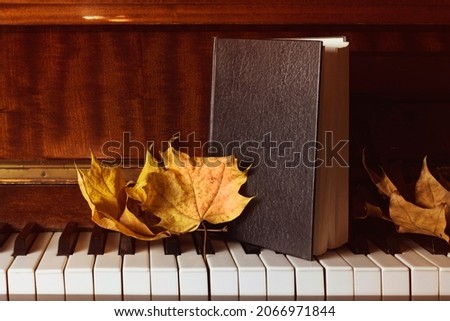 A large black book in a leather cover, similar to the Bible on the keys of an ancient piano. Ancient book and autumn yellow leaves on the piano Royalty-Free Stock Photo #2066971844
