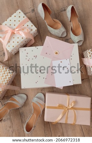 Photo of Blank white card in pink envelope isolated woodden color background with glitter stars, vaucher, gift certificate. White and pink backgroundamong woman shoes