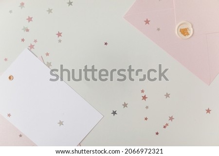 Photo of Blank white card in pink envelope isolated woodden color background with glitter stars, vaucher, gift certificate. White and pink background 
