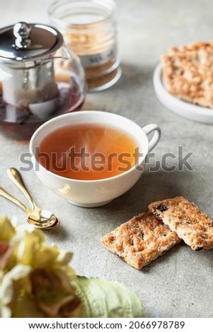 Hot steamed tea and two cookies on textured green background. Still life with a cup of tea, two cookies, a teapot, golden teaspoons and flowers. Vertical orientation Royalty-Free Stock Photo #2066978789