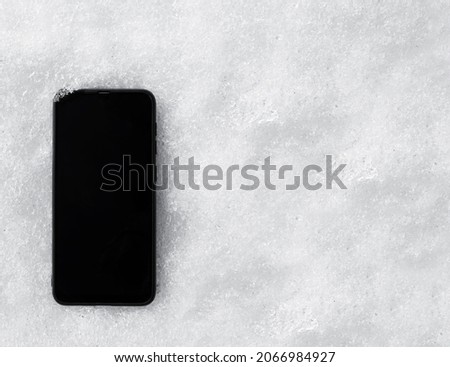 modern cell mobile phone (broken) lies on the white snow background. black blank and mock up. Winter season.
