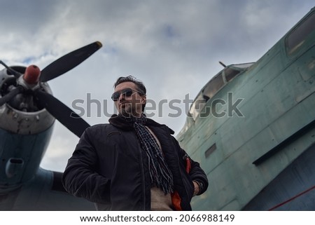 Oldschool pilot in the bomber jacket posing near the aircraft, aviator male with scarf and sunglasses Royalty-Free Stock Photo #2066988149