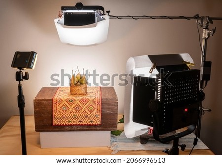 Horizontal behind-the-scenes view of professional ambient studio lighting setup for a food product photography session. Fruit is photographed with led lights in a small studio setup 