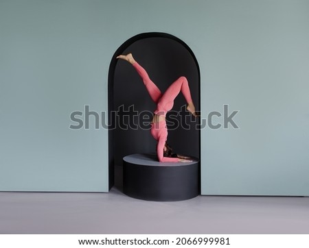 A woman is engaged in yoga doing a headstand. Yoga studio banner. Cyan background and pink sportswear. Trendy concept podium and arch. Gym stretching workout. Asana sport. Trainer coach