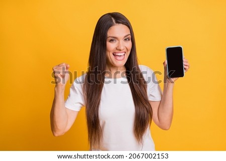 Photo portrait of woman showing smartphone touchscreen with copyspace gesturing like winner isolated on bright yellow color background