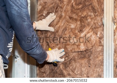The worker insulates the walls with mineral wool for further cladding with plasterboard. Heat insulation and sound insulation of housing. Royalty-Free Stock Photo #2067015032
