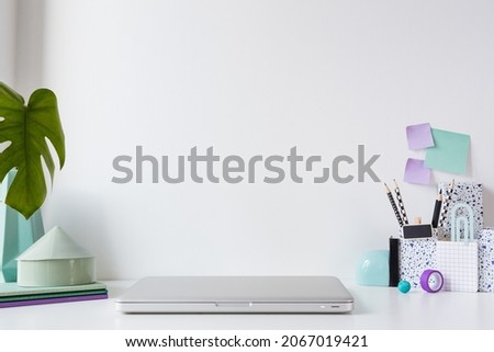 Home office. Table with closed laptop, books and supplies in purple colour. Stylish creative mock up with wall copy space.