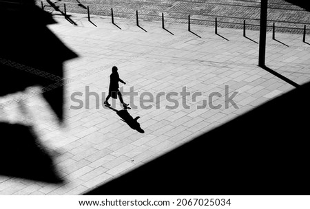 Shadow silhouette of a woman walking city street sidewalk square, in black and white from above with architectural shades Royalty-Free Stock Photo #2067025034