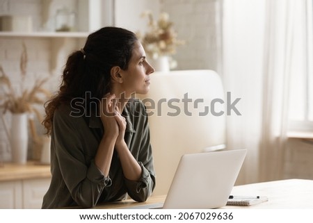 Serious pensive woman sit in kitchen at table with opened laptop looks into distance thinking, ponder, distracted from telecommuting, search for solution, daydream alone at home. Modern tech concept Royalty-Free Stock Photo #2067029636