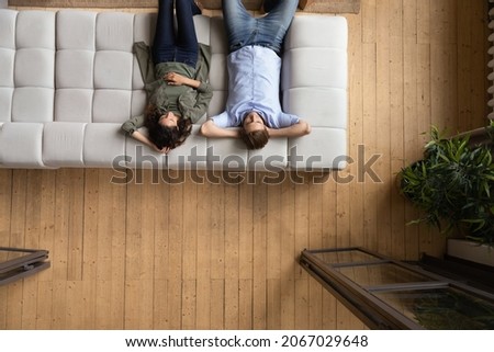 Serene couple put hands behind head relaxing on cozy sofa, above view. Homeowners family enjoy rest on fashionable furniture, breathing fresh conditioned air inside modern living room. Tenant concept Royalty-Free Stock Photo #2067029648