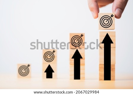 Hand putting target board which printing on wooden cube block on up arrow for enhance and set up business objective target  goal concept.