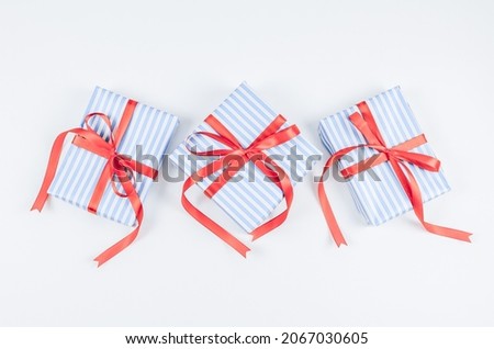 Three gift boxes in blue stripes with red ribbons in the middle on a white.