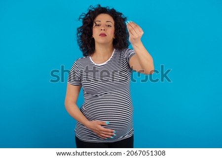 Young pregnant arab woman wearing striped T-shirt on blue studio background Doing Italian gesture with hand and fingers confident expression