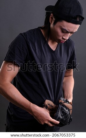 Asian male model with baseball glove isolated on dark background. Baseball player concept