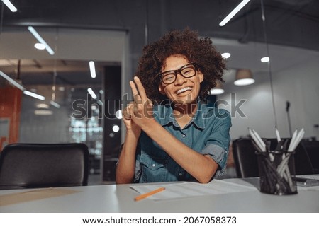 Smiling African American lady talking with sign language while sitting at her workplace in the office