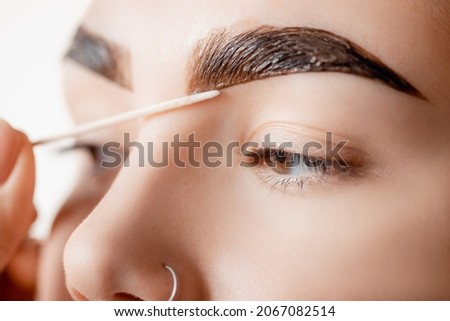 Correction and tint henna of eyebrows, master applies brush to woman marking on brow. Royalty-Free Stock Photo #2067082514