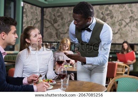 Hospitable African American waiter talking with young couple visiting restaurant Royalty-Free Stock Photo #2067085256