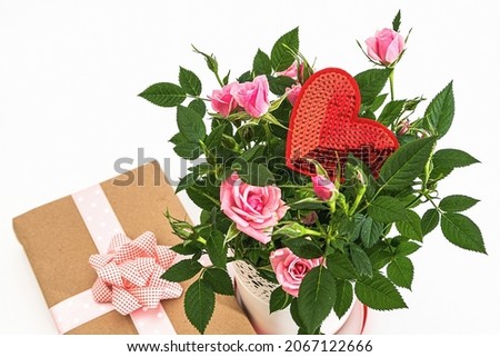 Bouquet of roses in a white vase, valentine card and a gift in wrapping paper on a white background. View from above.