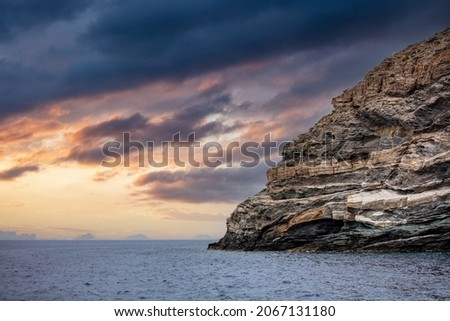 Tamelos cape at sunset Tzia island, Cyclades summer destination Greece. Stormy colorful cloudy sky over Kea huge rocky cliff empty Aegean ripple sea. Space.