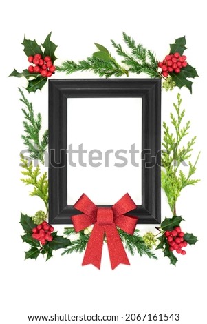 Christmas abstract background with wooden frame, red glitter bow, holly, ivy, mistletoe and fir leaves. Winter Xmas and New Year festive composition. On white, top view, copy space.
