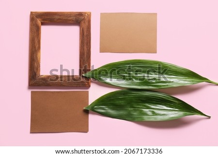 Composition with blank cards, empty picture frame and green leaves on color background