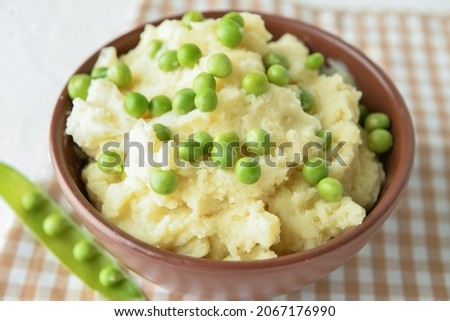 Bowl with mashed potatoes and green peas on table, closeup