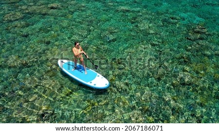 Aerial view of young girl stand up paddling on vacation. Tracking shot of a young woman SUP boarding.