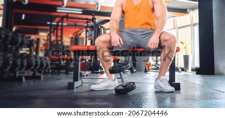 Close up of athletic man is sitting on a sports bench. The dumbbell lies near the athlete's feet. Sport banner.