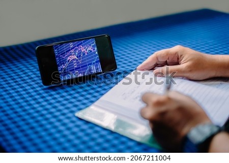Photo of man writing and cell phone showing candlestick chart