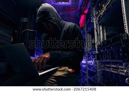 Hacker seated in server room launching cyberattack on laptop Royalty-Free Stock Photo #2067215408