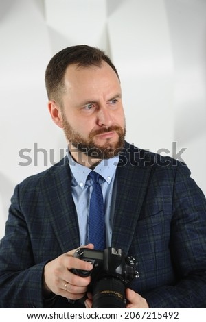 A man of European appearance with a beard with a camera. Business dress, shirt, tie, jacket. Commercial photographer for a business meeting, conference, reportage.