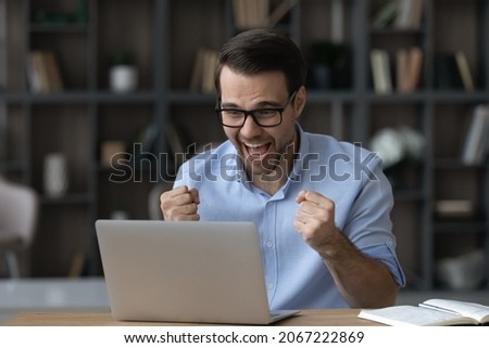 Overjoyed young businessman manager in glasses celebrating online lottery auction betting win, making successful profitable deal, feeling excited looking at computer screen in modern home office room. Royalty-Free Stock Photo #2067222869