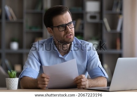 Stressed young businessman in eyewear feeling nervous of getting bad news in paper correspondence, reading letter with bank loan rejection or bankruptcy notification, having financial problems. Royalty-Free Stock Photo #2067223196