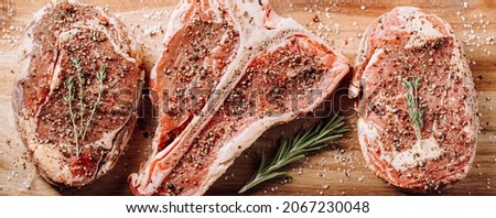 three lovely raw marbled black Angus beef steaks flavored with a mixture of ground pepper and ready to cook and serve on a dark wooden background.