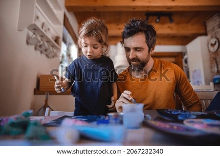 Mature father with small daughter resting indoors at home, painting pictures.