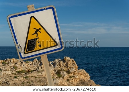 Close-up of a danger sign for people falling down a ravine, crooked. In the background the Mediterranean Sea on the island of Mallorca at sunset Royalty-Free Stock Photo #2067274610