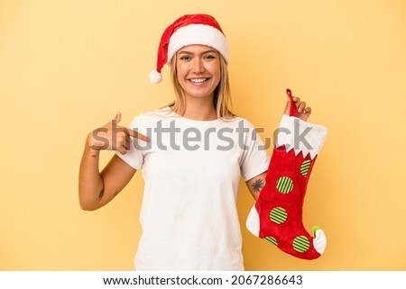 Young caucasian woman holding a elf sock isolated on yellow background person pointing by hand to a shirt copy space, proud and confident